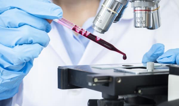 Selective focus of Scientist or doctor hands wear medical protective gloves looking at blood samples under microscope. Medical healthcare technology and pharmaceutical research and development concept.