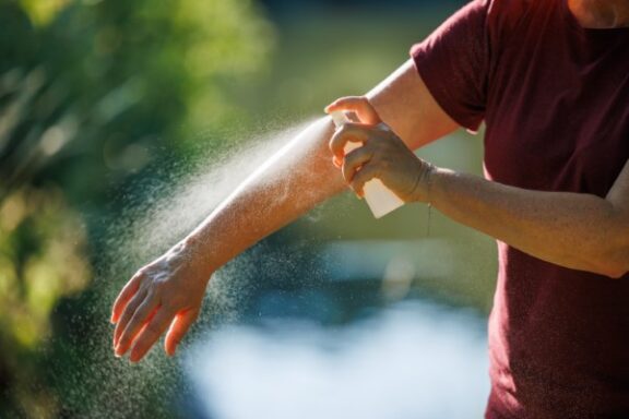 Woman applying insect repellant on her arm outdoors. Skin protection against tick and mosquito bite